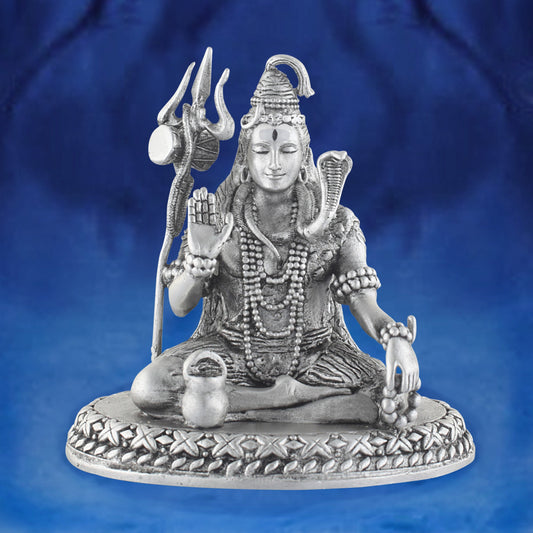 Silver statue of a seated shiva with a trident on a blue background