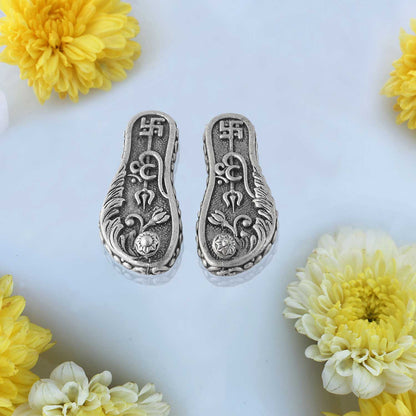 Silver paduka with floral designs on a white background with yellow flowers.