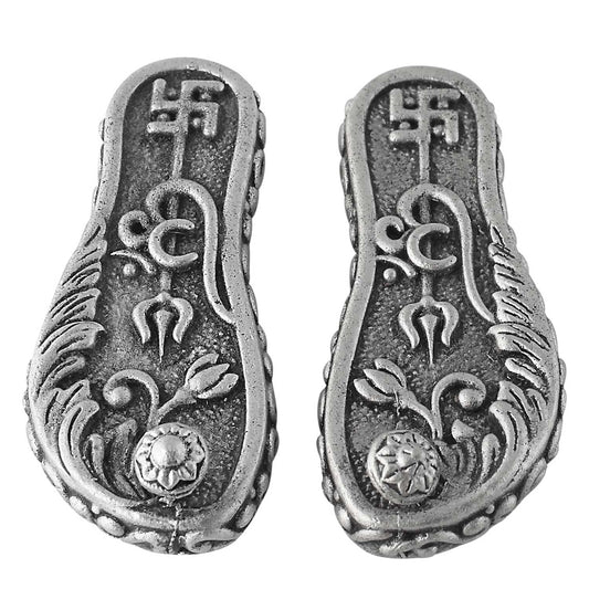 Pair of silver caharan paduka with intricate designs on a white background