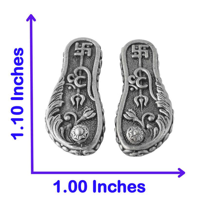 Pair of silver laxmi paduka with intricate designs and measurements on a white background