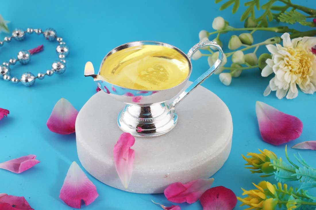 Silver diya with ghee on a blue background with flowers and petals