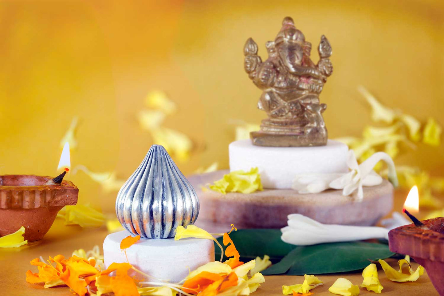 Decorative setup with a statue, candles, and flowers on a yellow background